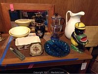 Overview of lot items displayed together showing Black Americana figurine, glass pitcher, ceramic bowls, Greek-style vase, and other items