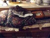 View of assorted picture frames and folded bed linens showing floral patterns and frames including wooden and metal types