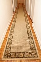 Full length view of the hall runner carpet showing the beige center with small dotted pattern and decorative floral border in earth tones.
