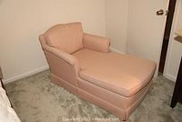 Side angle view of the pink upholstered lounger showing cushioned seat, backrest, armrests, and fabric skirt base.