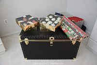 Black storage trunk loaded with Christmas decor boxes and wrapping paper rolls.