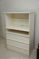Front view of white baby dresser/changing table showing three drawers below two open shelves.