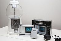 Full lot showing white gumball machine next to Ravinia atomic projection alarm clock with original box, remote sensor, and power adapter.