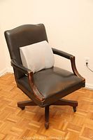 Black leather swivel desk chair with wooden armrests and base, showing wear and a tear on the seat.