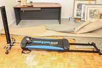 Side view of Total Gym Six exercise machine on parquet floor showing sliding board and metal frame.