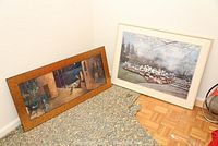 Two framed wall art prints pictured on the floor: one wooden framed with abstract art and one white framed with floral garden scene.