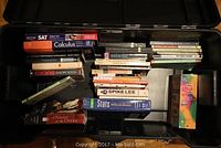 Top view of open black plastic bin showing various assorted books including SAT prep, calculus, statistics, and music-related titles.