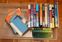 Plastic bin filled with various educational books laid open and stacked vertically showing titles on shelf and some lying flat.