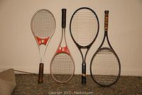 Four tennis rackets arranged standing against a wall showing different brands and grips