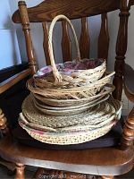 Stack of woven baskets and placemats shown on wooden chair, various shapes including oval with handles and round placemats.