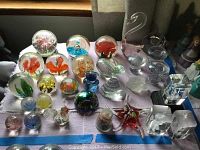 Overview of multiple glass paper weights on a striped cloth with varied colors and forms including spherical and abstract shapes.