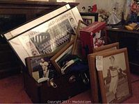 Photo showing assortment of framed photos, Red Sox World Champions print, folded shirts in a container, glass cups, and other memorabilia on a cabinet