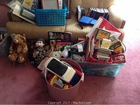 Full view of bins and containers holding toys, books, coloring materials, and plush toys arranged in front of sofa.