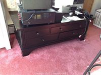Full view of black wooden TV entertainment center with five drawers placed on carpeted floor, supporting electronic equipment on top.