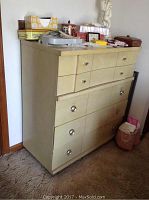 Front angle showing full 5 drawer dresser with items on top and cream/beige finish.