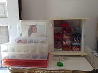 Wide shot showing stacked plastic storage containers and a cream-colored jewelry cabinet with compartments filled with costume jewelry items including earrings and necklaces.