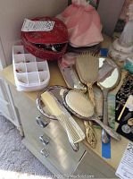 Photo of vintage hand mirrors, hairbrushes, combs, along with red bag of costume jewelry.