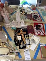 Overview of religious items including statues, crosses, rosary beads, medals, and prayer books arranged on a table with tape markings.