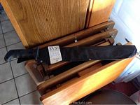 Machete in protective black sheath resting on wooden chair backs with tile floor visible