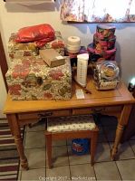 Photo of wooden sewing table with drawers and matching cushioned stool, various sewing accessory containers including floral storage boxes, jars of buttons, threads, and small boxes.