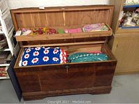 Photo of cedar hope chest open showing interior shelf tray with assorted textiles and crocheted items inside, demonstrating storage capacity.
