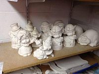 Photo of unpainted ceramic elf on the shelf figurines, sleeping cats, dancing couple, mouse with present figurine on a shelf