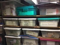 Three shelves of plastic storage bins labeled with holiday and household categories