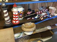Wide shot of shelf containing American eagle emblem jar, wooden lighthouse figurines, and red, white, and blue patriotic decor sticks.
