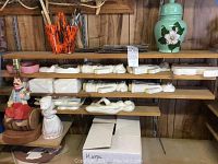 Shelf with finished ceramic figurines, ceramic jars, unfinished molds, and containers holding many brushes