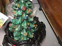 Two green ceramic Christmas trees with colored decorative flowers and butterflies shown atop black plastic bag, green glossy glaze, multi-colored translucent decorations all over, top bulb openings visible in second image.