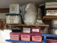 Photo showing multiple labeled plastic bins on shelves, white ceramic bust figures, and other craft supplies.