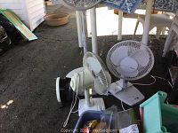 Three fans shown together: two white table fans with corded bases, and one large grey Lasko pedestal fan on adjustable stand.