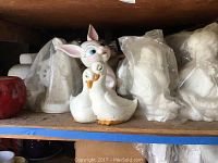 Shelf with painted ceramic rabbit and two ducks, and white ceramic figurines wrapped in plastic