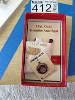 Box displaying pair of 14KT gold amethyst earrings, 14KT gold American flag pin, and sterling silver Cathedral of the Pines charm on original cards.