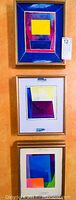 Full shot of the three framed abstract paintings displayed vertically on a wall, showing their size, frame style, and overall condition.