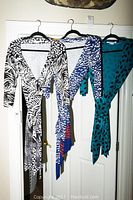Three Diane Von Furstenberg wrap dresses hanging on hangers showing front view with V-neck and waist ties.