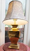 Single brass lamp with patterned bell-shaped fabric shade in natural light on a round table.