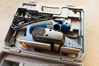 Ryobi Power Planer model HPL51 in open gray plastic carrying case with electric cord and attached planer body showing side view.