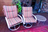 Two swivel patio chairs with striped cushions and a white metal mesh side table on a wooden deck.