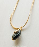 Close-up of gold chain with black onyx and diamond pendant on white surface.