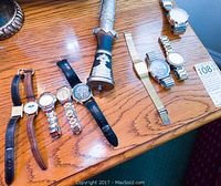 All 9 watches laid out on a wooden surface showing mixed metal and leather bands with various dial colors and styles.