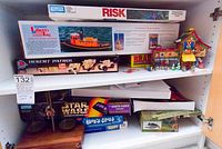 Photo showing shelf with boxed board games including Risk, Liberty Tug, Desert Patrol, Star Wars, Brain Quest, and Blue's Clues. Also includes a toy wooden house set and figurines.