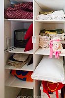 Overview of shelves with the Panasonic TV, linens including sheets, pillows, folded blankets, and a stuffed animal dog.