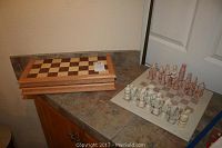 Photo showing two closed wooden chessboards stacked and a stone chessboard with carved stone chess pieces arranged for play.