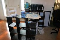 Two black shelving units with cubbies, white desk file organizers, 3-D framed maps, a globe, HP ink cartridges, and office cleaning sprays on and around the shelves.