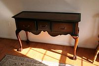 Front angled view of wooden dining room side table with three drawers and claw feet under natural lighting.