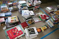 Wide view showing many stacks of books on floor, various subjects and formats.