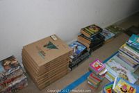 Books stacked in piles along a wall showing a mix of hardcovers and paperbacks