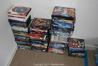 Multiple stacks of DVDs on carpeted floor showing a large number of titles and box sets of movies and TV shows in standard DVD cases.