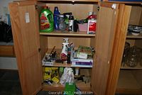 Wooden cabinet open showing shelves with various cleaning products, lightbulbs, and household items.